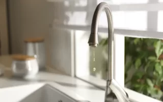 summer light shining through kitchen window where a kitchen sink faucet is slowly dripping water