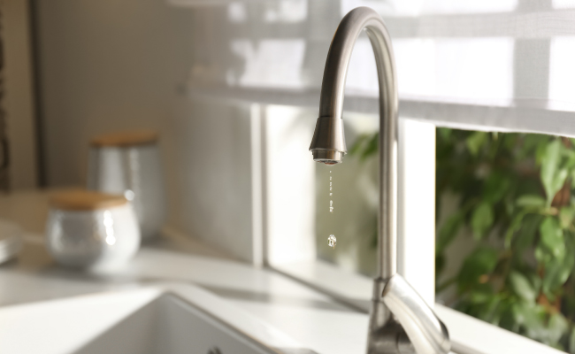 Light shining through kitchen window where a kitchen sink faucet is slowly dripping water.