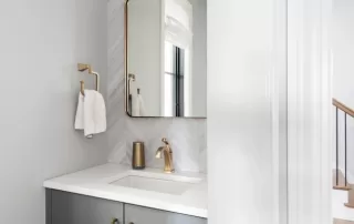 modern bathroom vanity with gold faucet, white countertops, and herringbone tile backsplash
