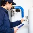 A plumber in a blue uniform checks and repairs a hot water heater.