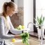 A young woman with blonde hair washes lettuce and vegetables in an elegant farmhouse style sink in her kitchen.